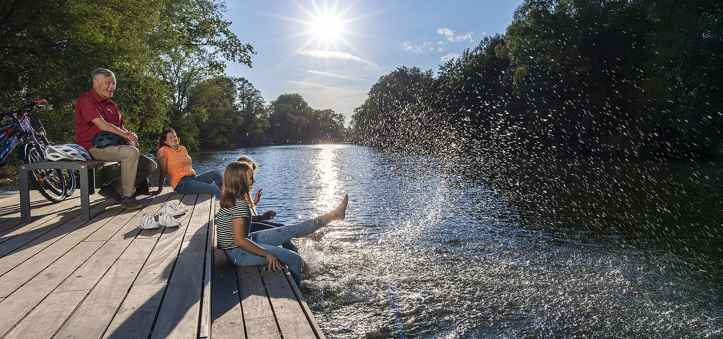 Radfahrende machen Pause am Wasser und plantschen mit den Füßen.
